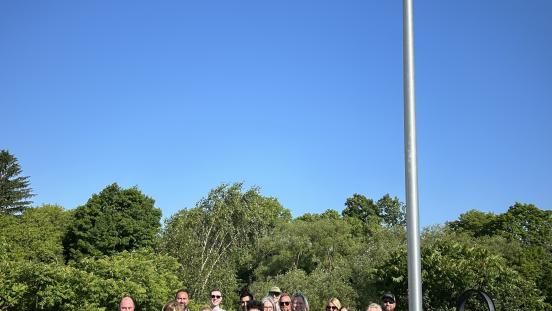 Town of The Blue Mountains staff and Council members stand beside a flagpole flying the Pride Flag. 