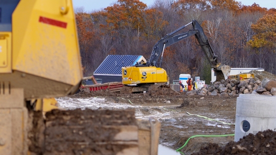 Excavator digging behind pile of boulders