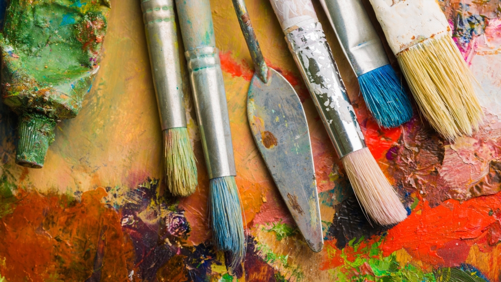 Paintbrushes and art supplies on paint-covered board