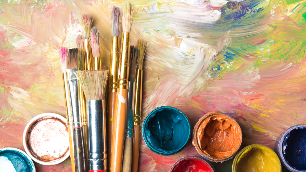 Paint cups and paint brushes spread across a colourful background