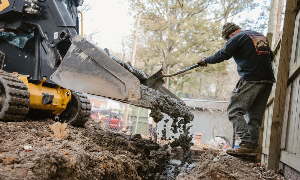 Skid steerer pouring concrete into backyard trench