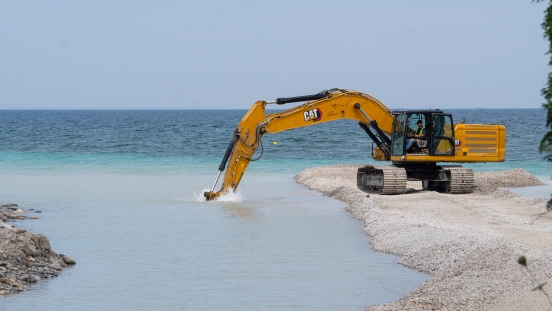 Excavator parked on gravel pier with bucket in water