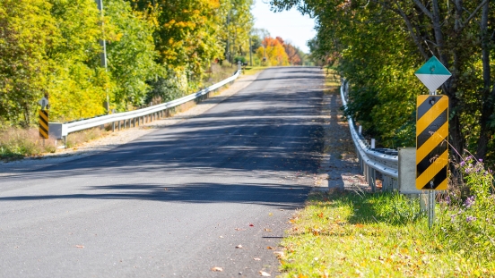 Guiderail and signage on paved road with fall foliage