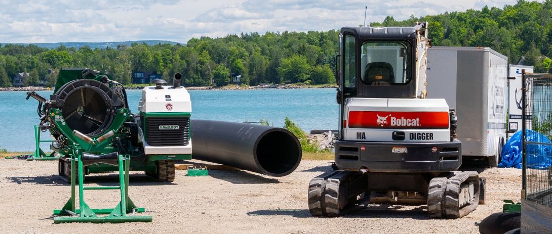 Pipe and fusing equipment staged on gravel laydown area with Bay in the background
