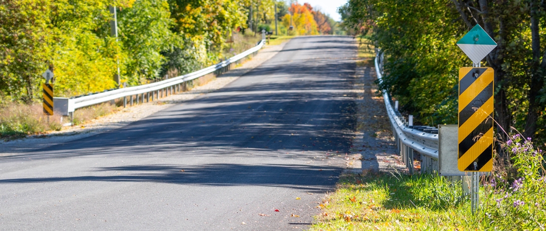 Guiderail and signage on paved road with fall foliage