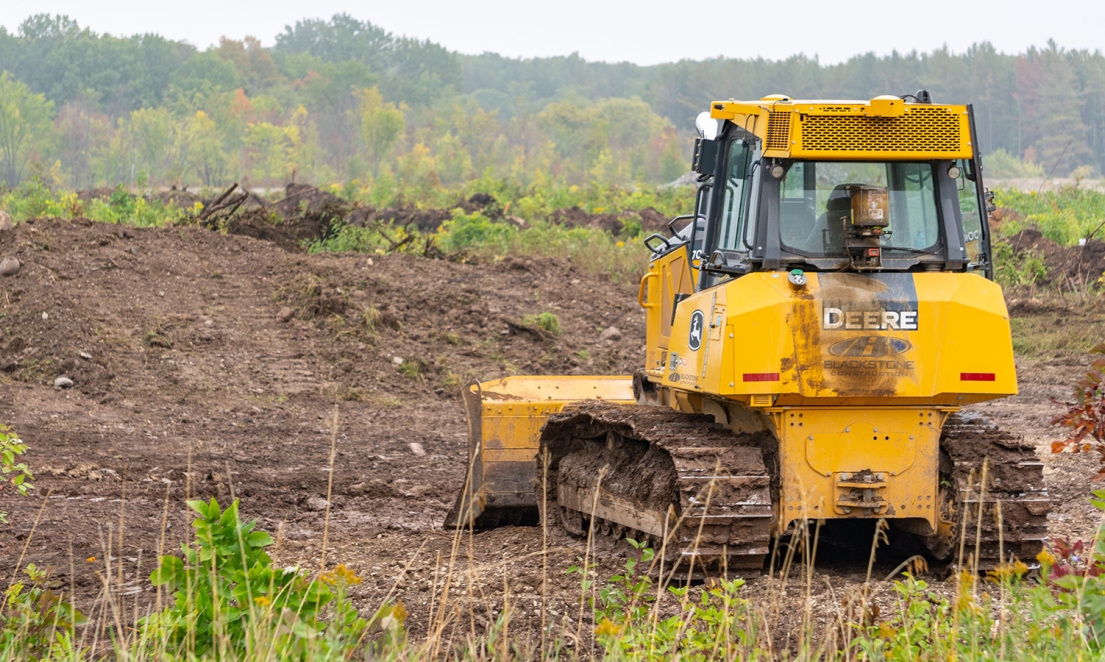 Bulldozer parked in front of pile of stripped topsoil