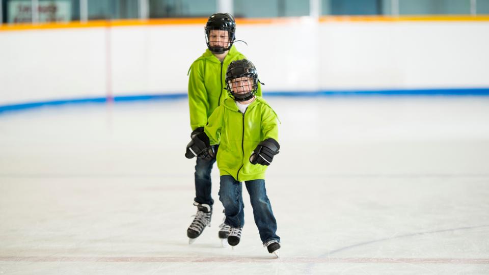 Two kids skating on an indoor ice rink