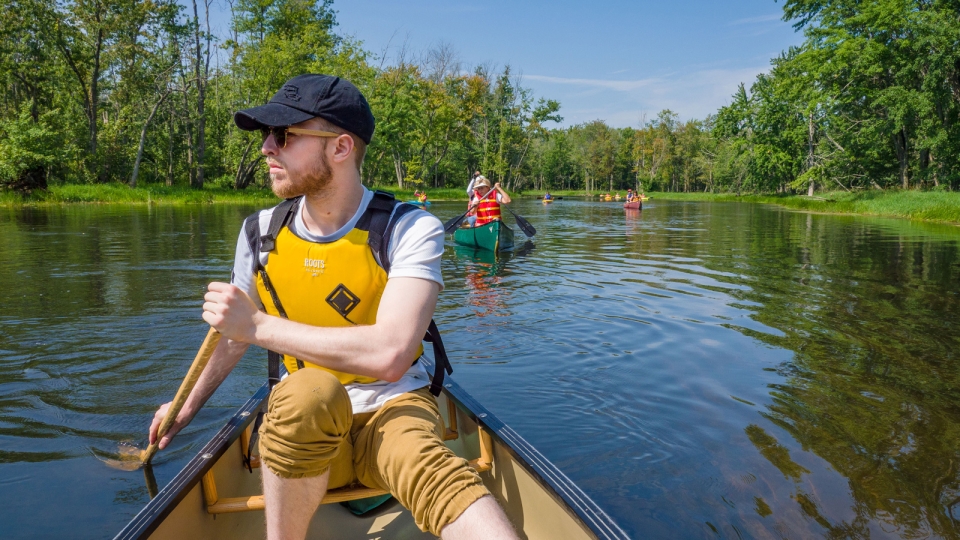 Man canoeing on river with people behind him